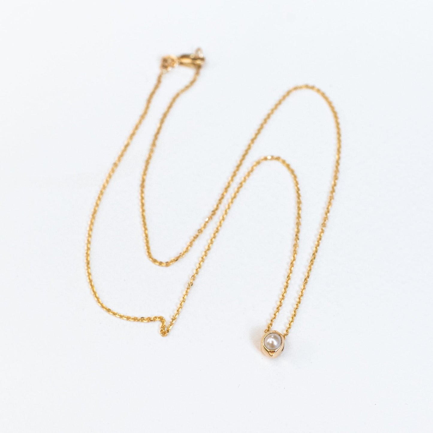 Hand detail showing oceanus pearl pendant close to skin, intimate luxury jewelry