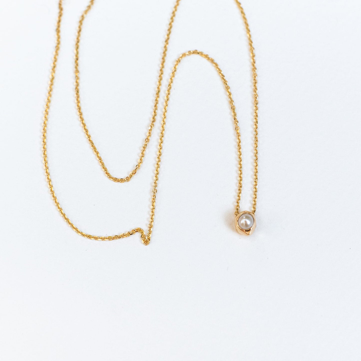 Model wearing oceanus pearl necklace layered with other delicate gold chains